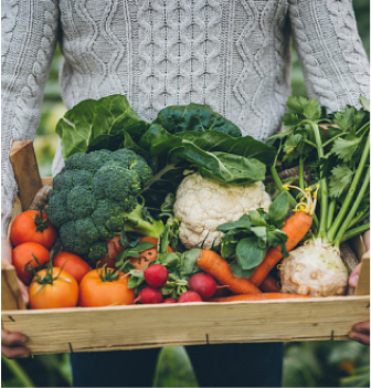 person holding a wood basket full of an assortment of fresh vegetables